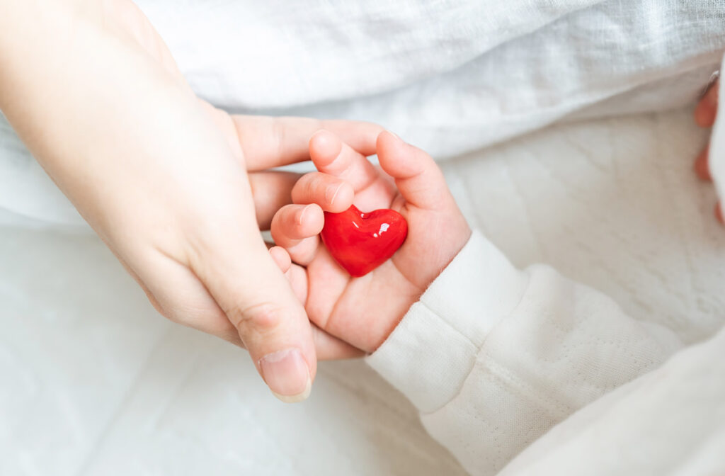donations Adult and baby hands holding a red heart, symbolizing love and care.